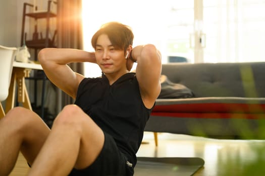 Strong asian man wearing sporty clothes doing sit up exercise during home workout. Sport, fitness and healthy lifestyle.