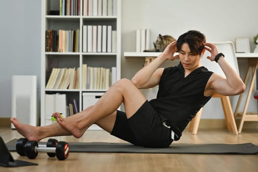 Sporty attractive man doing abdominal sit ups on mat at home. Fitness, training and healthy lifestyle concept.