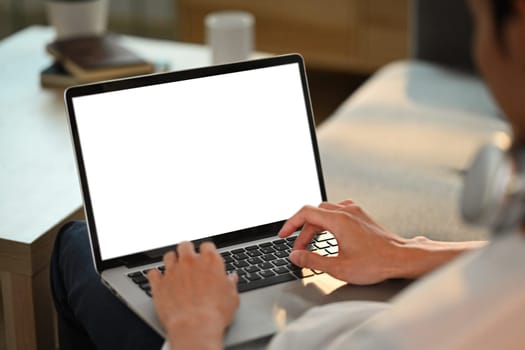 Cropped shot of man hands typing on keyboard of laptop, browsing internet on couch at home.