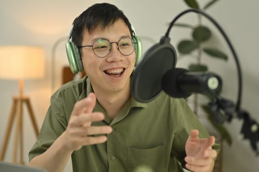 Smiling male podcaster talking into a microphone while streaming podcast from home studio.