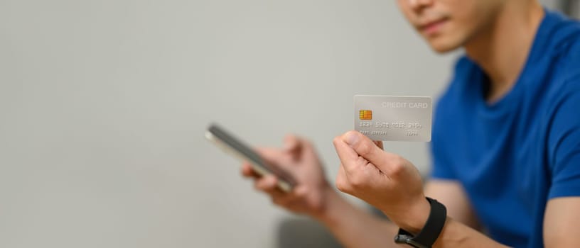 Man hand holding credit card and using smartphone for making online transactions or checking her bank account.