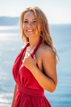 Smiling young woman in a red dress looks at the camera. A beautiful tanned girl enjoys her summer holidays at the sea. Portrait of a stylish carefree woman laughing at the ocean