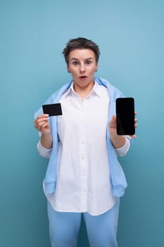 vertical photo of a stylish fashionable young lady with tousled hair in a white shirt with a credit card and a smartphone.