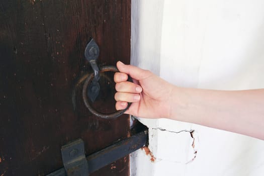 Female hand opens an ancient door. Vintage iron door handle in the form of a ring. Toned image