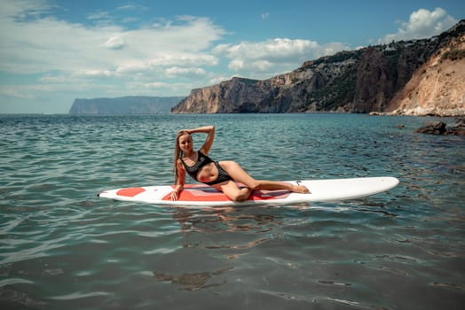 Woman sap sea. Sports girl on a surfboard in the sea on a sunny summer day. In a black bathing suit, he sits on a sapa in the sea. Rest on the sea