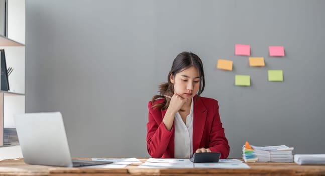 Asian woman business using a calculator calculating financial expense at home office.