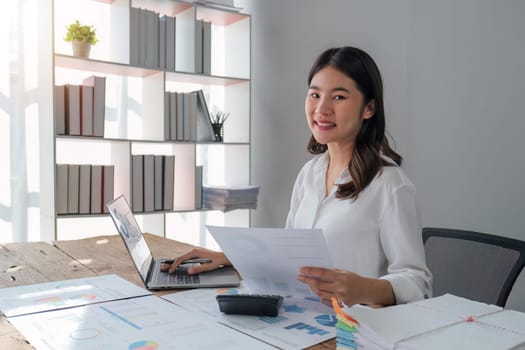 Asian businesswoman sit at their desks at office and calculate financial graphs showing results about their investments, plan a successful business growth process, diagrams on screen.