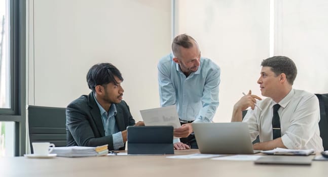 Business team discussing online project, showing computer presentation to skilled team leader. Friendly diverse colleagues working in pairs on laptop.