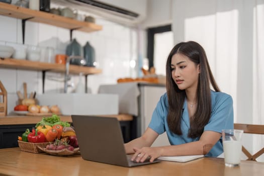 Asian young woman use laptop in the kitchen at home.