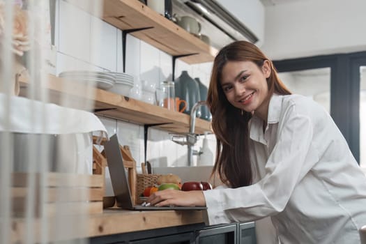 Asian young woman use laptop in the kitchen at home.