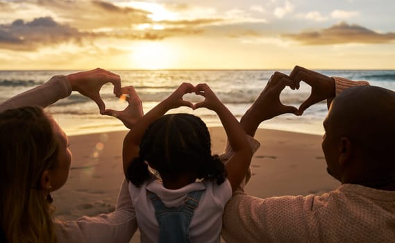 Beach, heart hands and family for love of summer, ocean and outdoor wellness with parents, child and sunset sky clouds . Behind of people, or mother and father with kid with care sign or icon for sea.