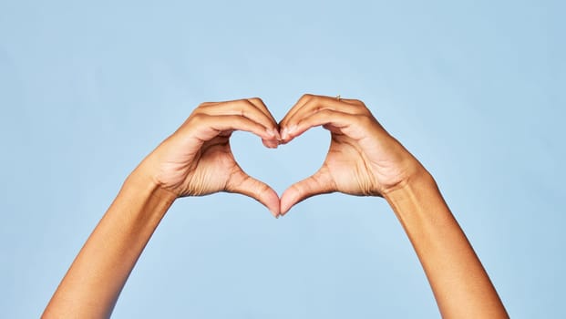 Hands, heart and emoji with a person in studio on a blue background for love, health or social media. Affection, romantic and hand gesture with an adult indoor to show a sign or icon of romance.