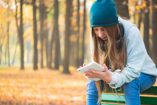 Cute girl using tablet on bench in autumnal park