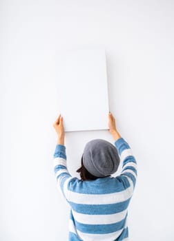 Girl holding blank canvas on white wall