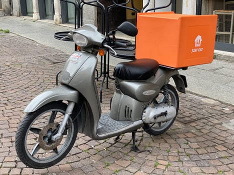 Lombardy, Italy - April 2023 just eat delivery scooter parked in center of town