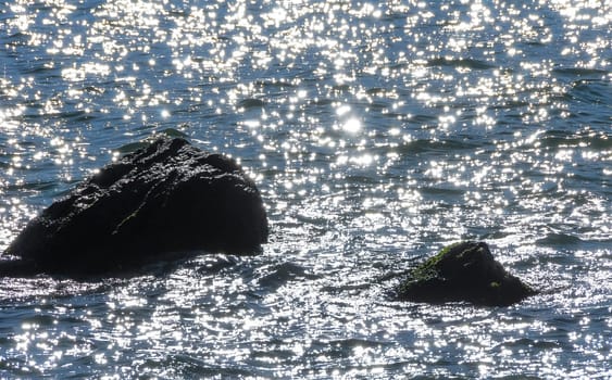 Bright reflections on the water on a sunny day among the coastal rocks near the Black Sea coast