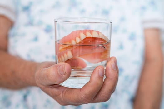 Asian senior woman patient holding and washing denture in water cleanser glass for good chewing.