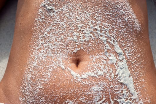 the sand of a tropical beach on the navel of a girl sunbathing