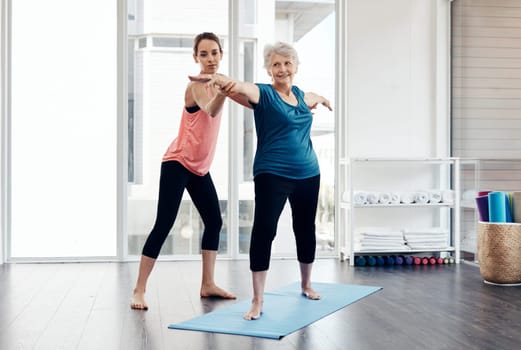 Yoga allows her to reach better health and wellness. a fitness instructor helping a senior woman during a yoga class