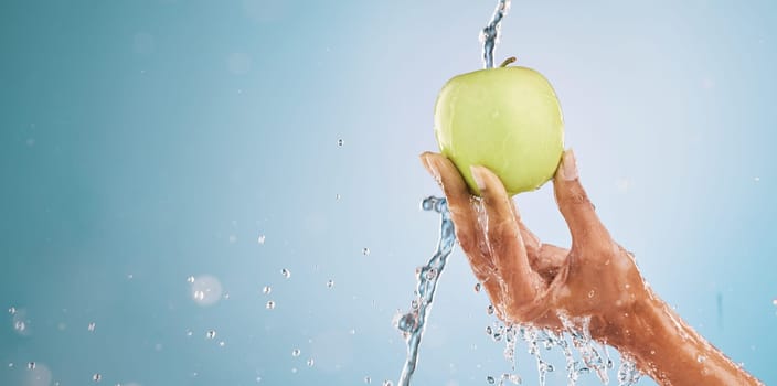Water splash, hand of woman and apple in studio on a blue background mockup. Fresh food, cleaning hygiene and female model washing fruit for healthy diet, vitamin c or nutrition, skincare or beauty