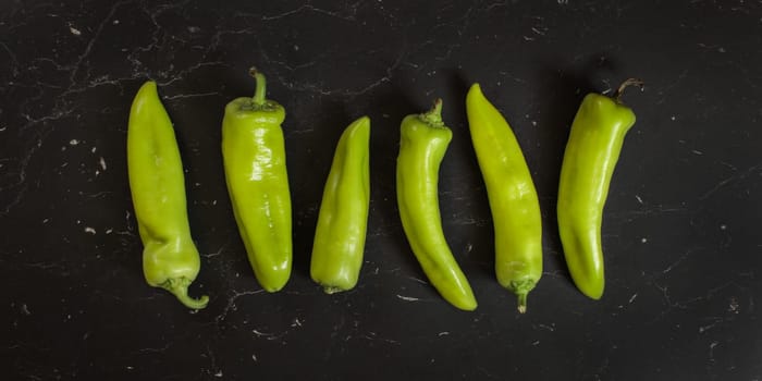 Top down view, green pointed peppers on black board.