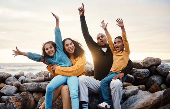 Black family, parents and kids in beach portrait with hands in air, sitting and rocks with celebration. Black woman, man and children by ocean with love hug, care and bonding on holiday by sunset sky.