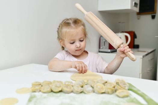 Little girl in flour prepares dumplings in the kitchen