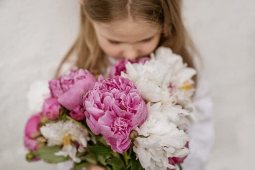 Portrait of a little girl smelling peonies