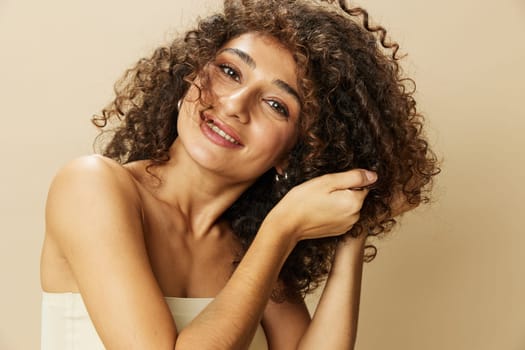 Woman applies cream and balm to her curly hair, the concept of protection and care, a healthy look, a smile with teeth on a beige background.