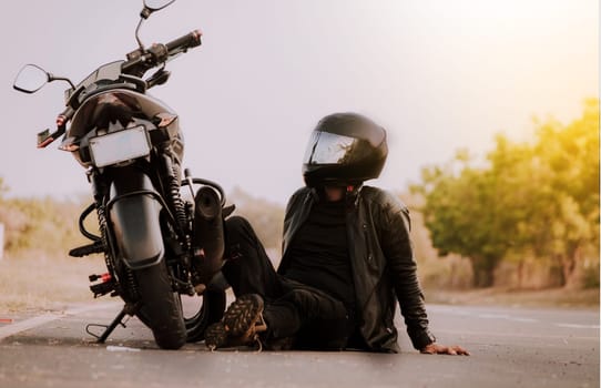 Motorcyclist sitting next to his motorcycle. Motorcyclist sitting and leaning on his motorcycle on the asphalt