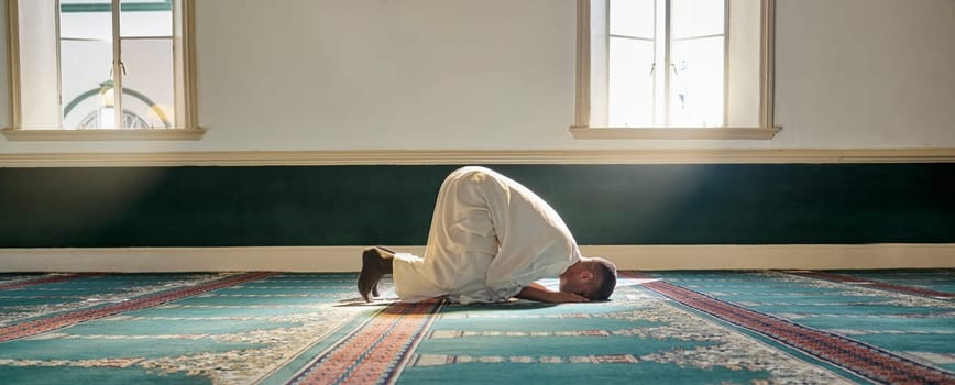 Mosque, worship and muslim man in prayer on his knees for gratitude, support or ramadan for spiritual wellness. Religion, tradition and islamic guy praying or reciting quran to allah at islam temple