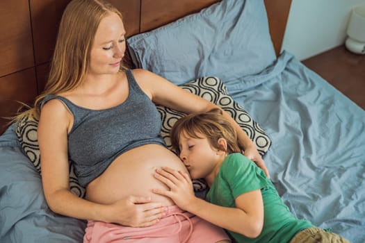 Young beautiful pregnant woman and eldest son. The cute boy leaned his ear against his mother's belly. Expecting a baby in the family concept. Preparing an older child for a younger one.