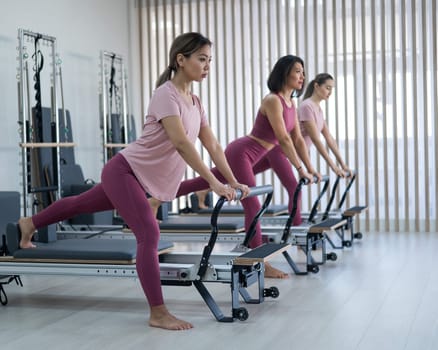 Three Asian women doing lunges on a reformer machine