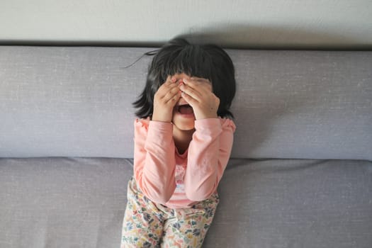 a upset child girl cover her face with hand .