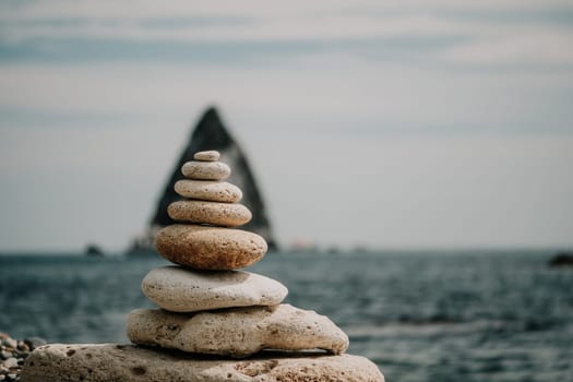 Pyramid stones on the seashore with warm sunset on the sea background. Happy holidays. Pebble beach, calm sea, travel destination. Concept of happy vacation on the sea, meditation, spa, calmness.