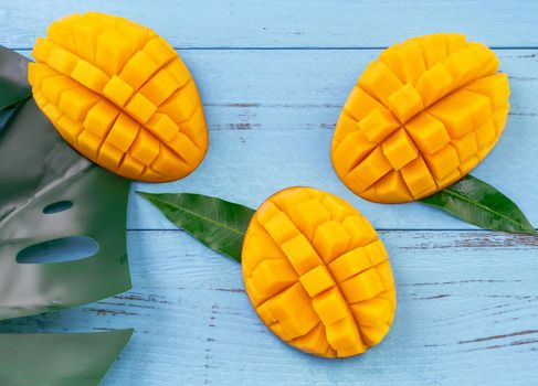 Fresh mango - beautiful chopped fruit with green leaves on bright blue timber background. Tropical fruit design concept. Flat lay. Top view. Copy space