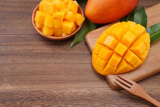 Fresh mango, beautiful chopped fruit with green leaves on dark wooden table background. Tropical fruit design concept. Flat lay. Top view. Copy space