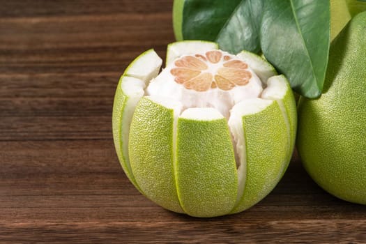 Fresh peeled pomelo, grapefruit, shaddock with green leaves on dark wooden plank table. Seasonal fruit near mid-autumn festival, close up, copy space