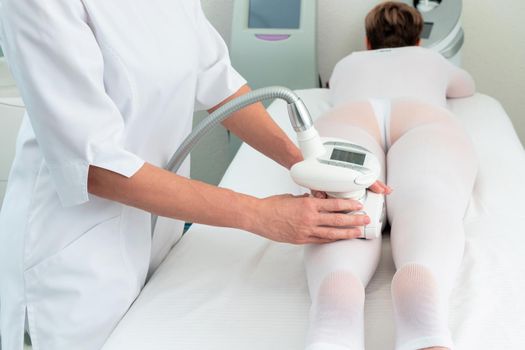 Woman in special white suit getting anti cellulite massage in a spa salon. LPG, and body contouring treatment in clinic