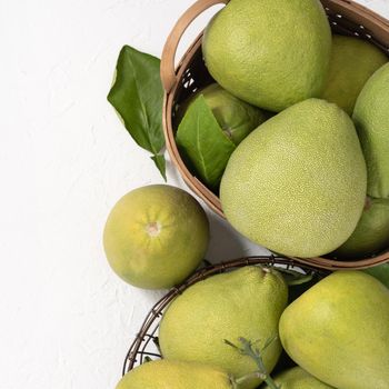 Fresh pomelo, grapefruit in bamboo basket with green leaf on bright white background. Seasonal fruit for Mid-Autumn Festival. Top view. Flat lay.