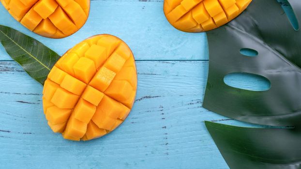 Fresh mango, beautiful chopped fruit with green leaves on dark wooden table background. Tropical fruit design concept. Flat lay. Top view. Copy space