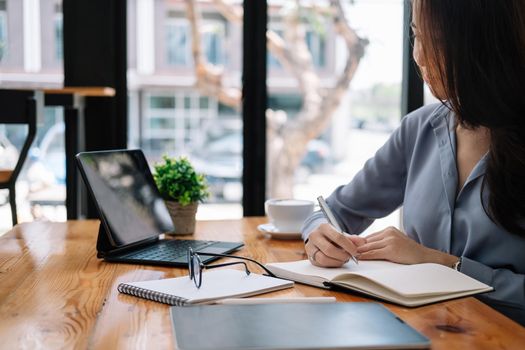 business asian woman hand taking notes with various items placed on the office table. online meeting, online learning concept.