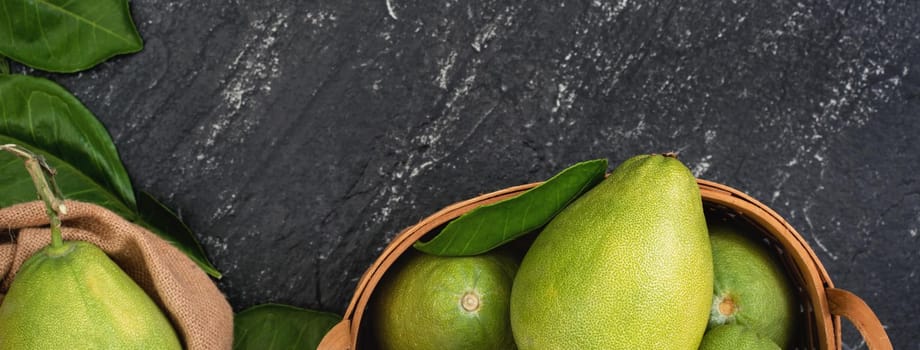 Fresh pomelo, pummelo, grapefruit, shaddock in bamboo basket with leaf on dark black slate background. Seasonal fruit concept. Top view. Flat lay.