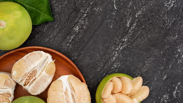 Fresh pomelo, pummelo, grapefruit, shaddock in bamboo basket with leaf on dark black slate background. Seasonal fruit concept. Top view. Flat lay.