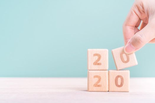 Abstract 2020 & 2019 New year countdown design concept - woman holding wood blocks cubes on wooden table and green background, close up, copy space.