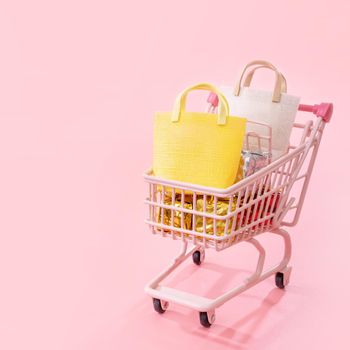 Annual sale shopping season concept - mini red shop cart trolley full of paper bag gift isolated on pale pink background, blank copy space, close up