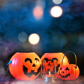 Halloween concept - Orange plastic pumpkin lantern on a dark wooden table with blurry sparkling light in the background, trick or treat, close up.