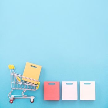 Abstract design element, concept of annual sale, shopping season - mini yellow cart with paper bag isolated on pastel blue background, top view, flat lay.