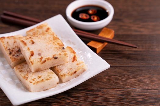 Delicious turnip cake, Chinese traditional local dish radish cake in restaurant with soy sauce and chopsticks, close up, copy space.