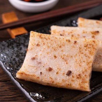 Delicious turnip cake, Chinese traditional local dish radish cake in restaurant with soy sauce and chopsticks, close up, copy space.